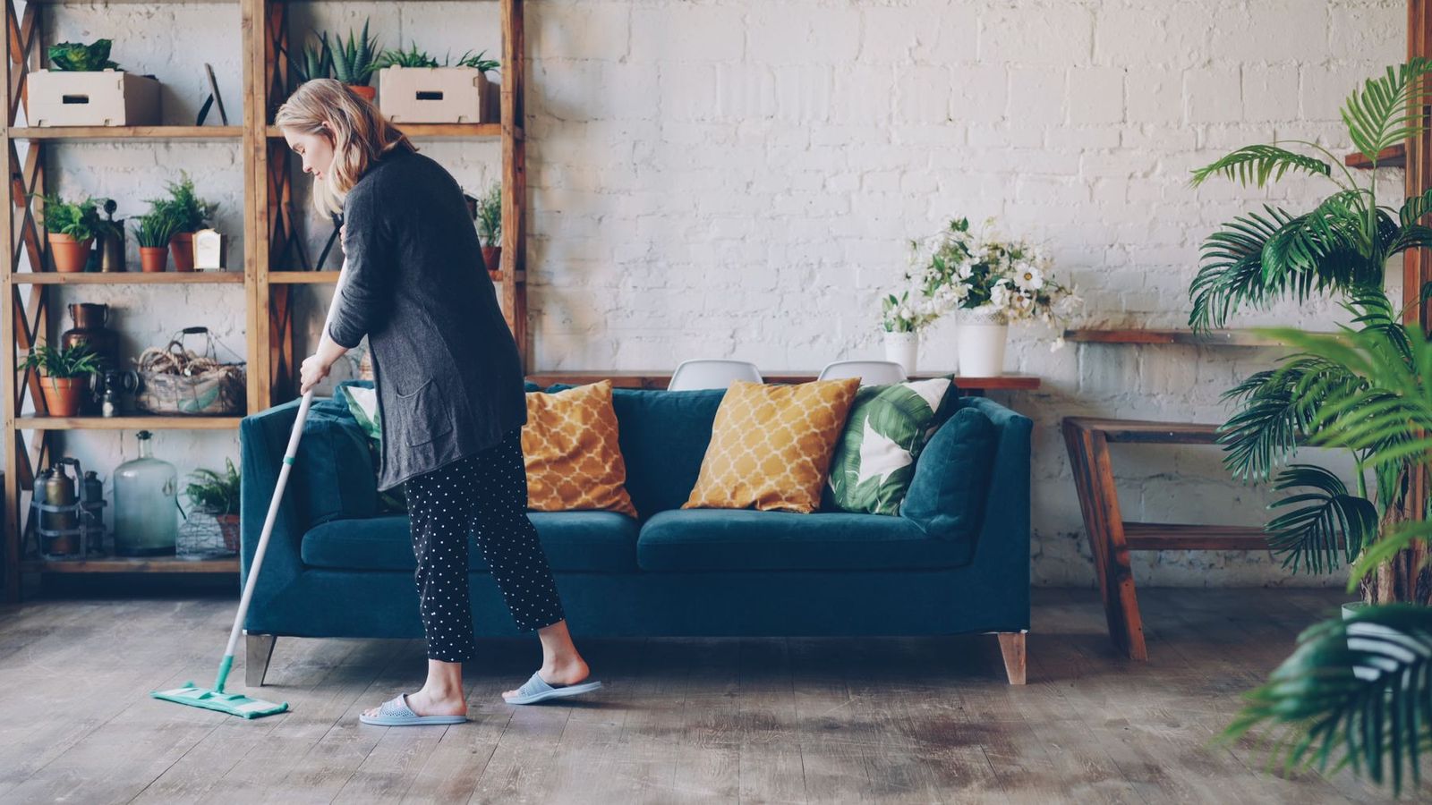 Frau wischt mit dem Mopp ein Wohnzimmer mit blauem Sofa